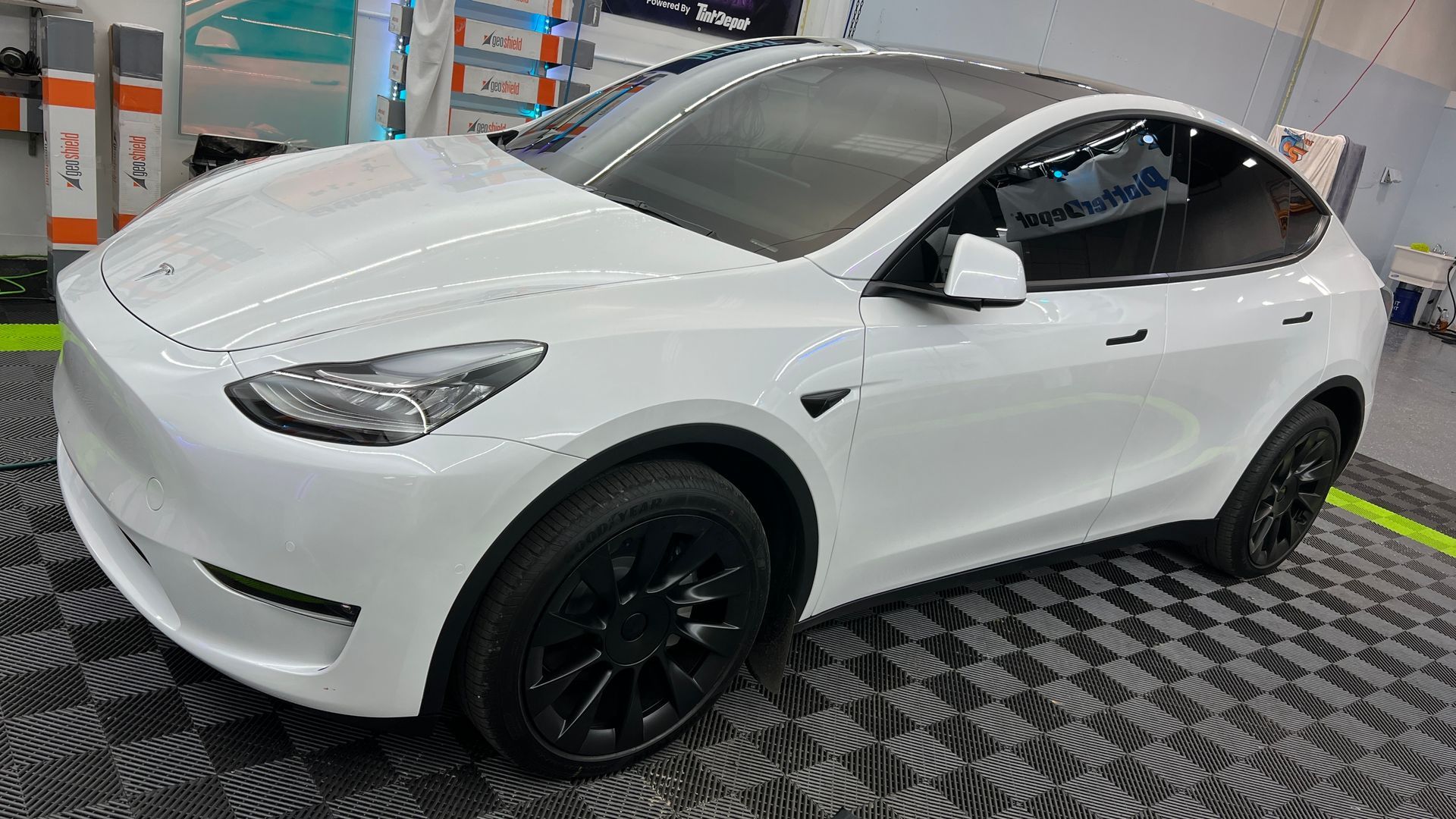 a white tesla model y is parked on a checkered floor in a garage .