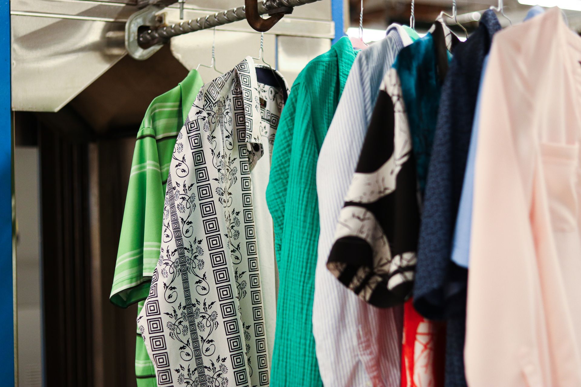 Clothes hanging on a rack: green striped shirt, patterned shirt, teal shirt, striped shirt, and other colorful shirts.