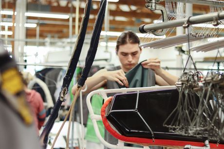 A young person inspecting fabric on a machine in a factory setting.