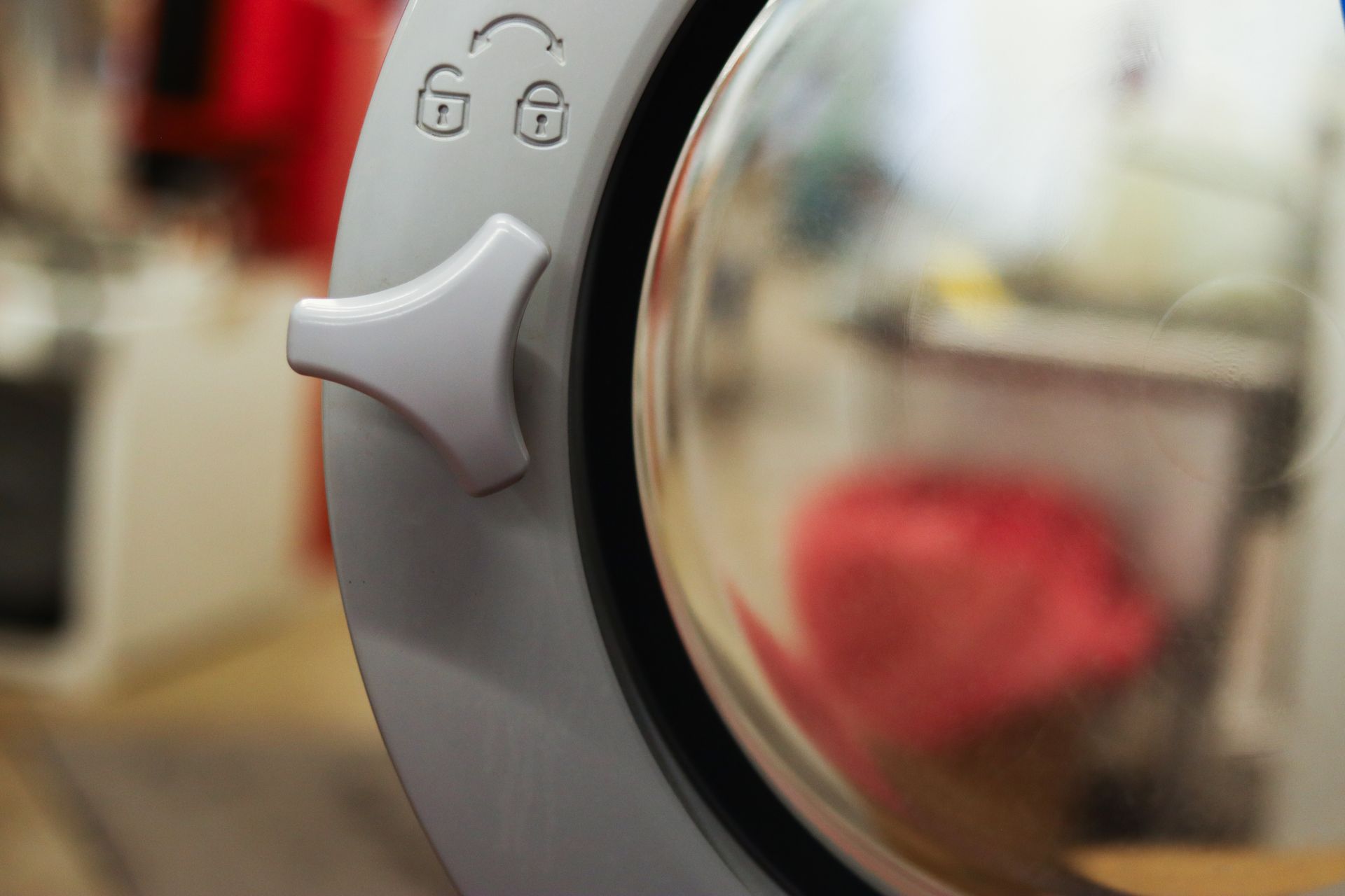Washing machine door close-up, white handle on gray panel, glass door, locked symbol.