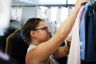 Woman in glasses hanging a pink shirt on a rack of clothes.