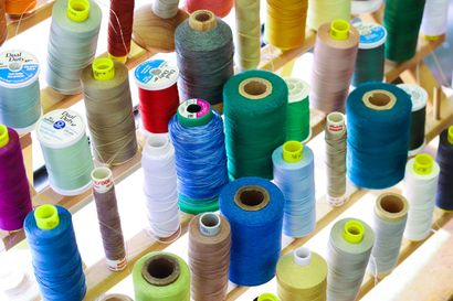 Spools of colorful thread arranged on a wooden shelf; various colors, textures, and sizes.