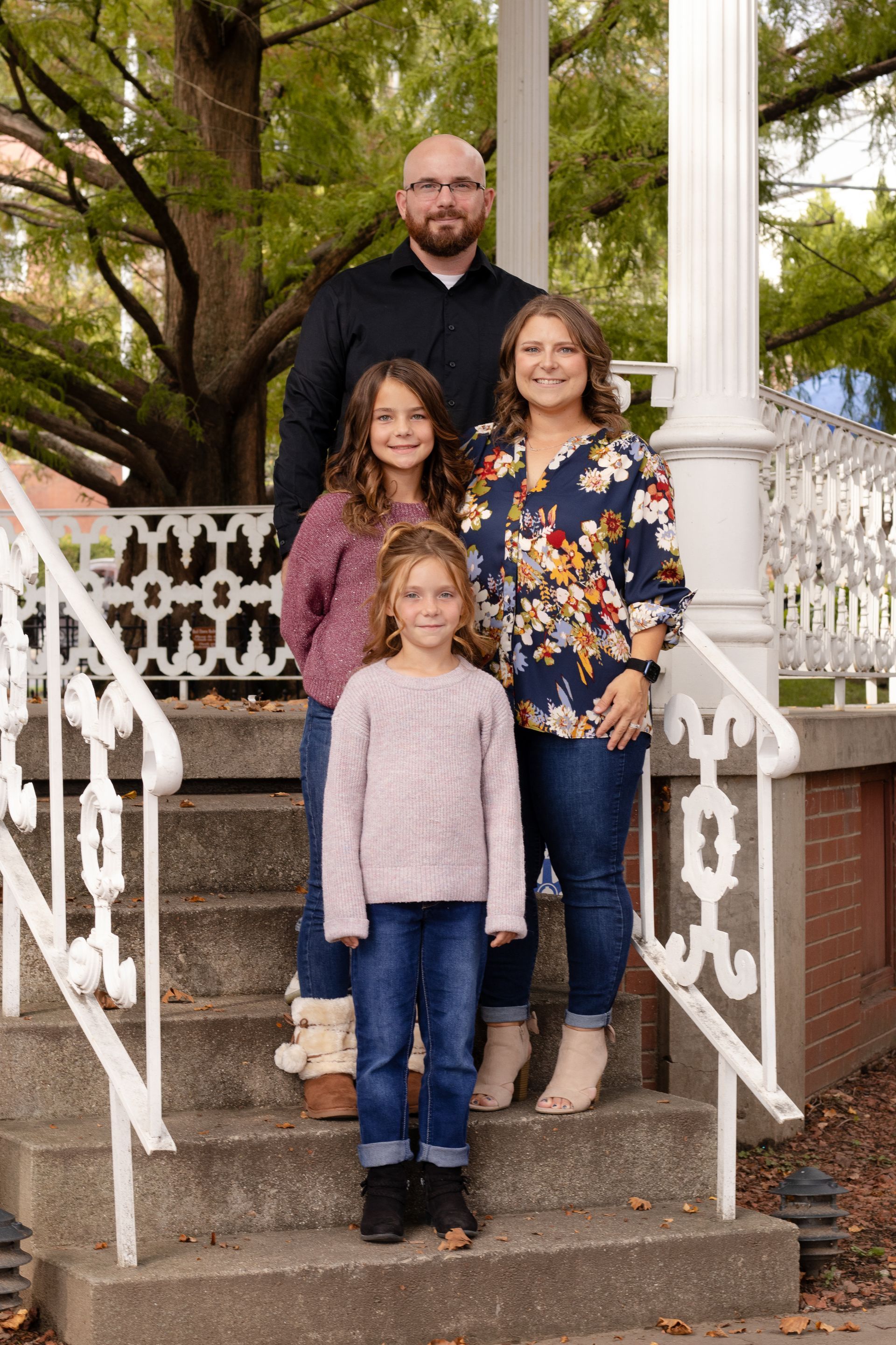 Family of four smiling on steps in front of white gazebo.