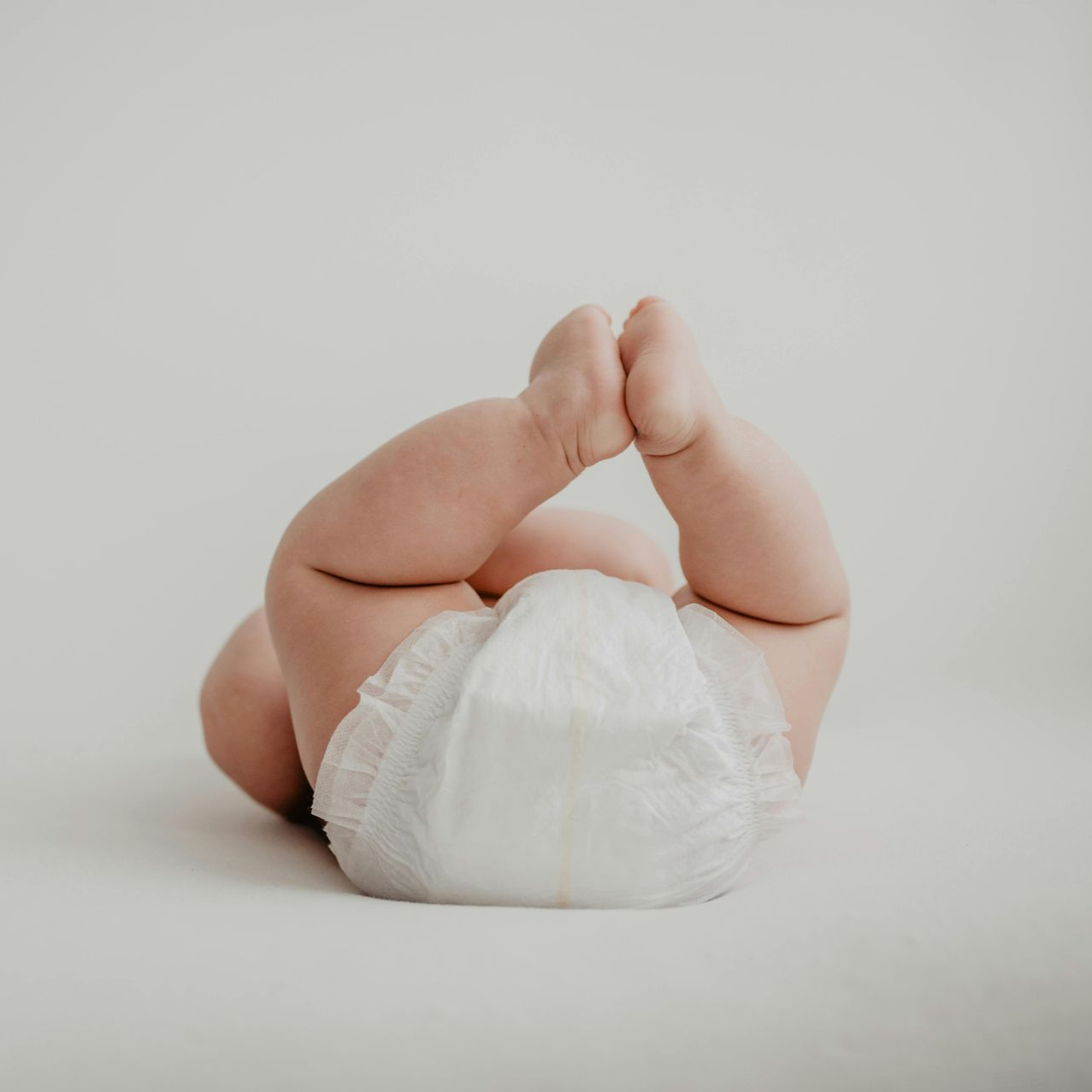 Baby lying on stomach with feet touching, wearing a diaper, on a white background.