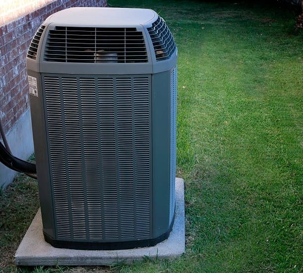 Gray outdoor air conditioning unit on a concrete pad, surrounded by grass.