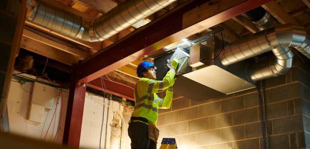 Construction worker in safety gear working on air ducts in a building's basement.