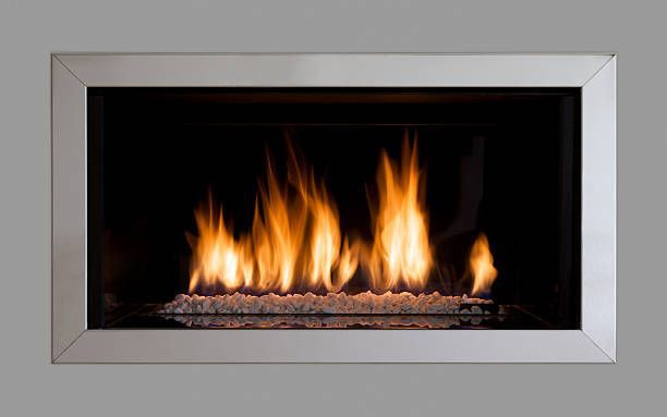 Gas fireplace with flames and glass pebbles, set in a stainless steel frame against a dark background.