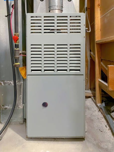 A gray furnace unit in a basement setting, with vents and a round access door.