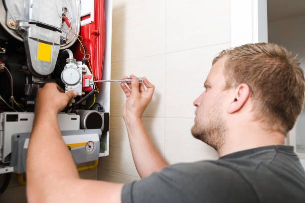 Man repairing a boiler with a screwdriver; white wall, indoor setting.