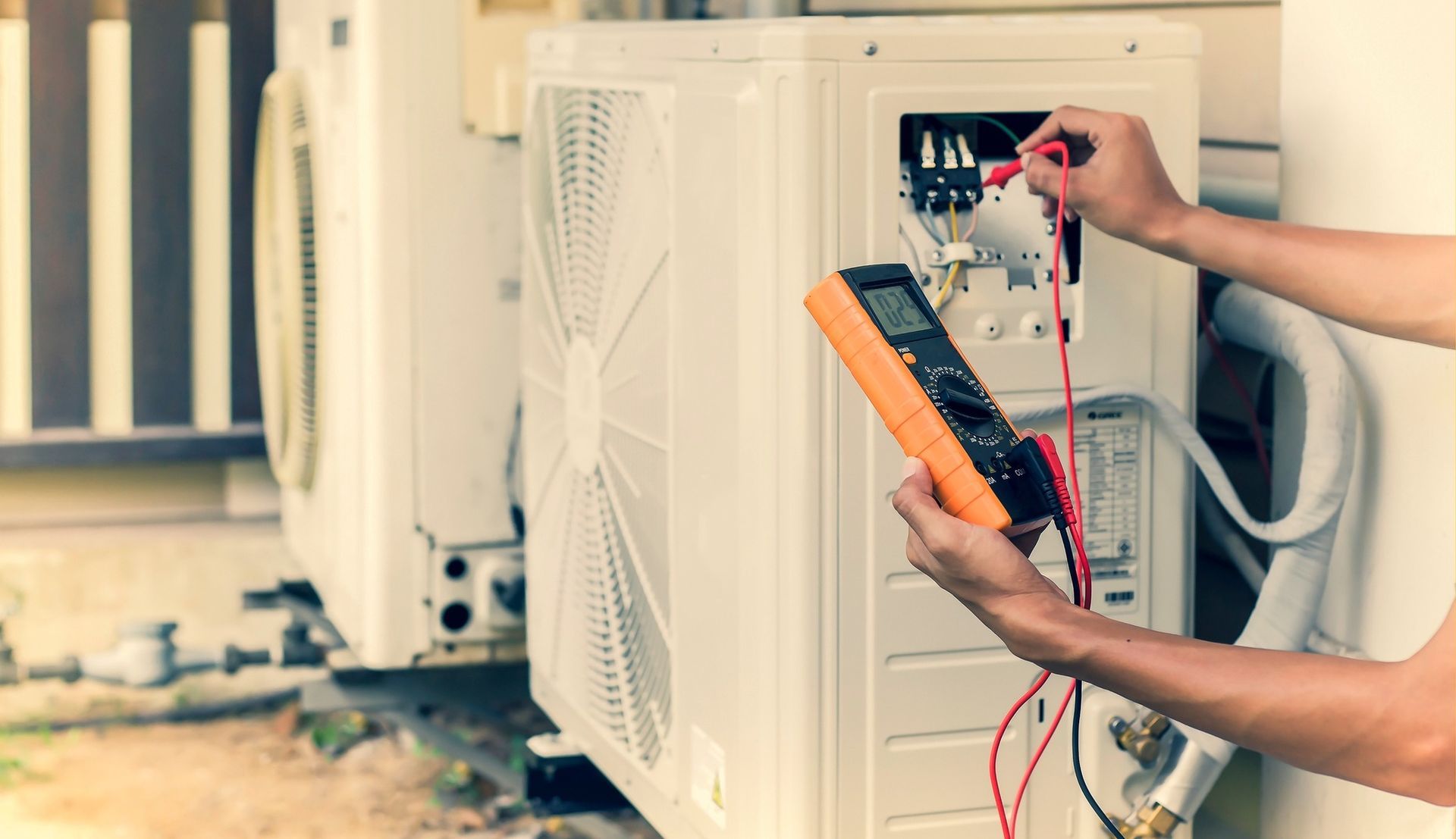 Person testing an air conditioning unit with a multimeter.