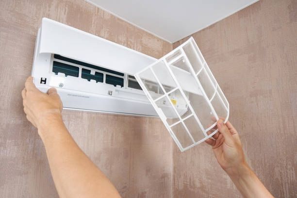 Person removing an air conditioner filter from a wall-mounted unit.