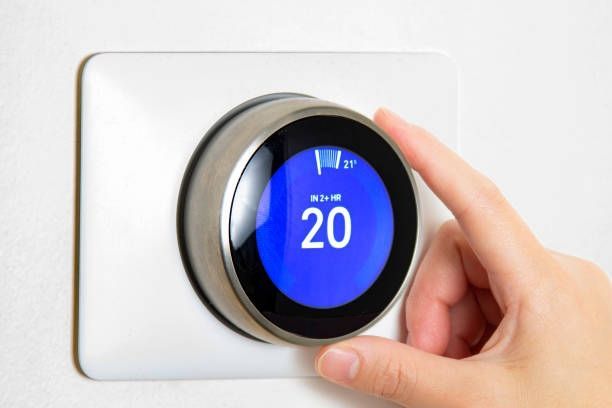 Hand turning a smart thermostat dial, setting temperature to 20 degrees Celsius.