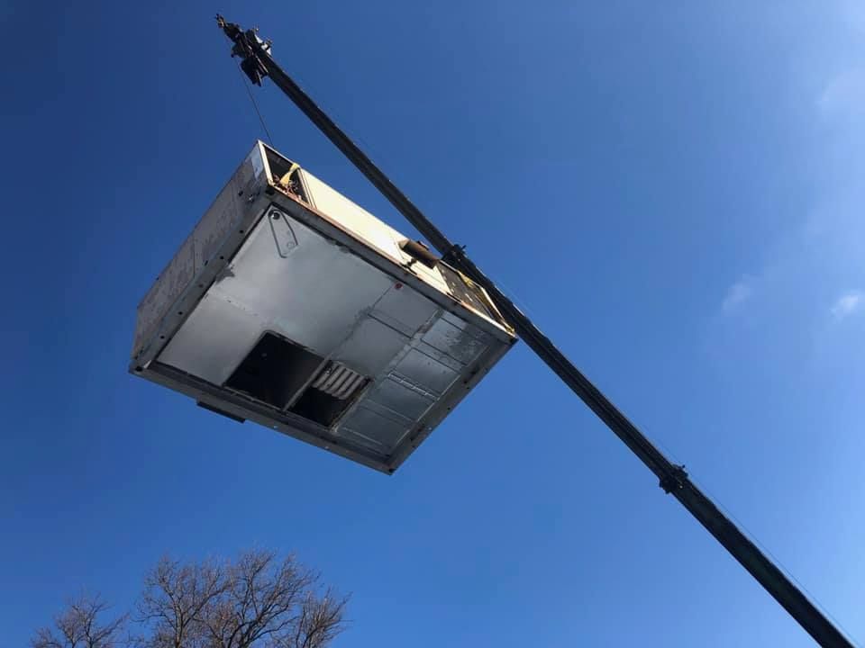White and black heat pump unit outside next to a brick wall.