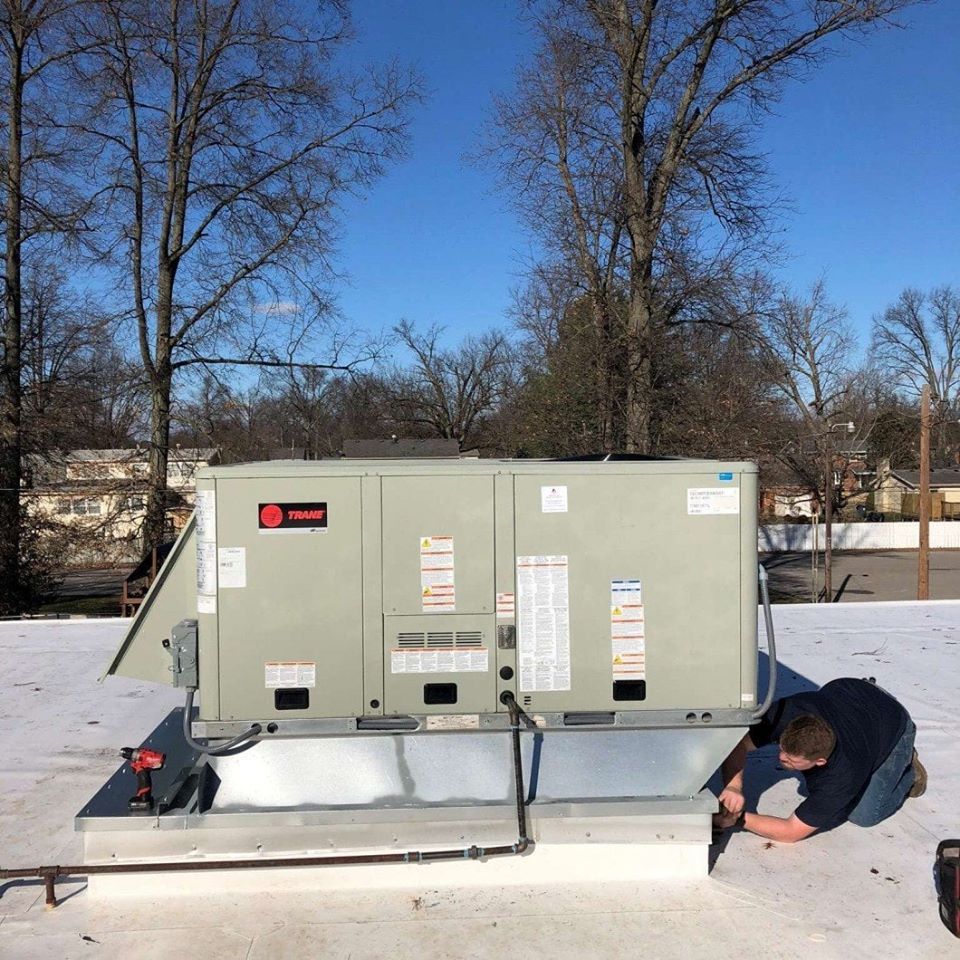 Person using a screwdriver to service a white wall-mounted air conditioner unit.