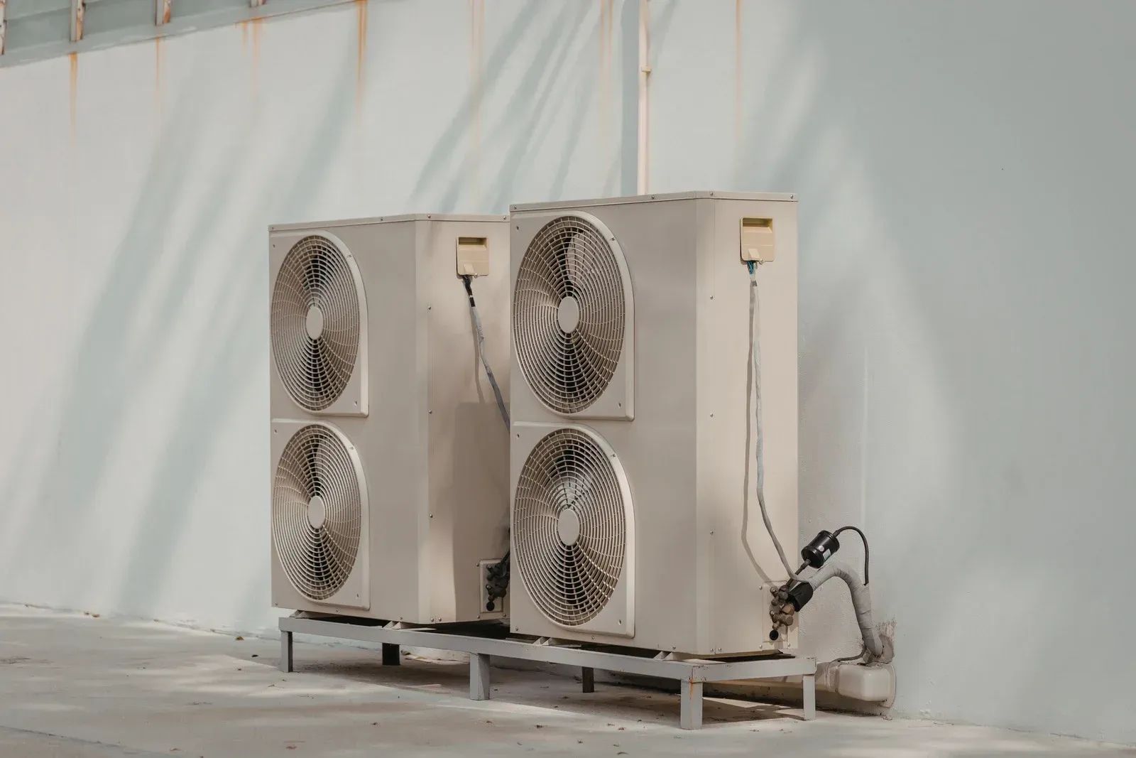 Two large beige industrial outdoor units with fans, mounted on a pallet against a white wall.