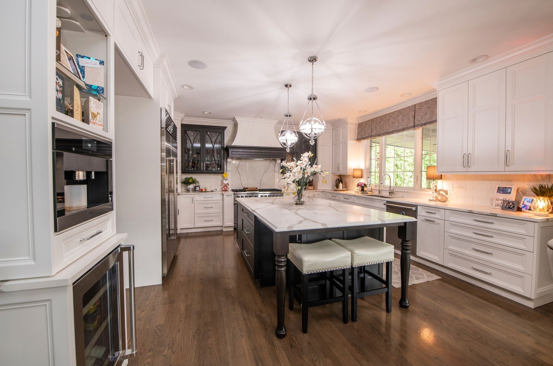 A modern, white kitchen with a large island, hardwood floors, and white cabinetry.