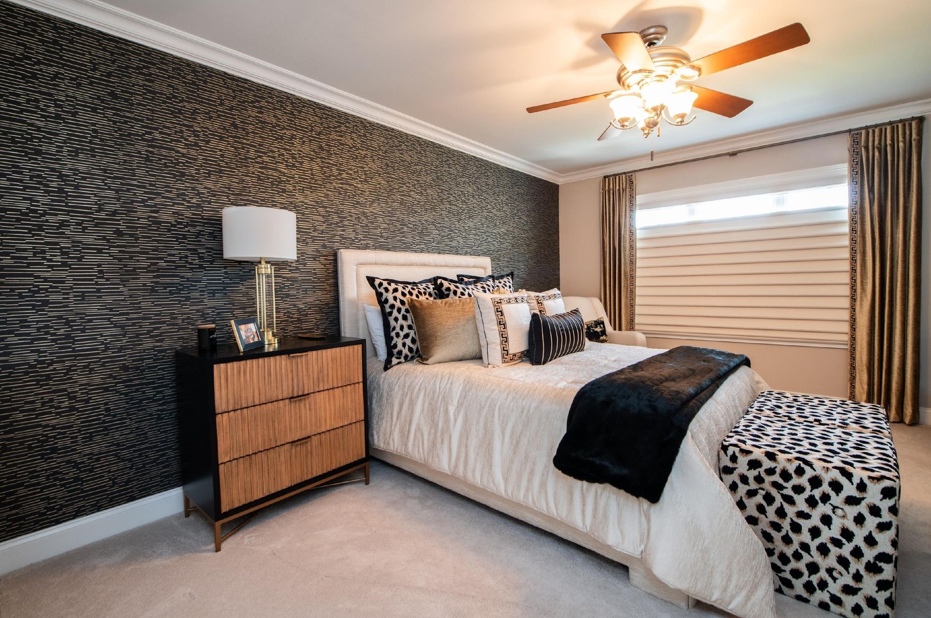 Bedroom with patterned wallpaper, bed with pillows and a black throw, nightstand.