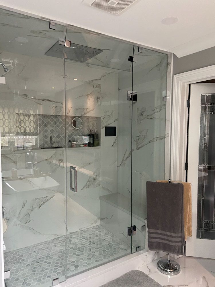 Glass-walled shower with marble tiling, a towel, and a door. Bathroom setting.