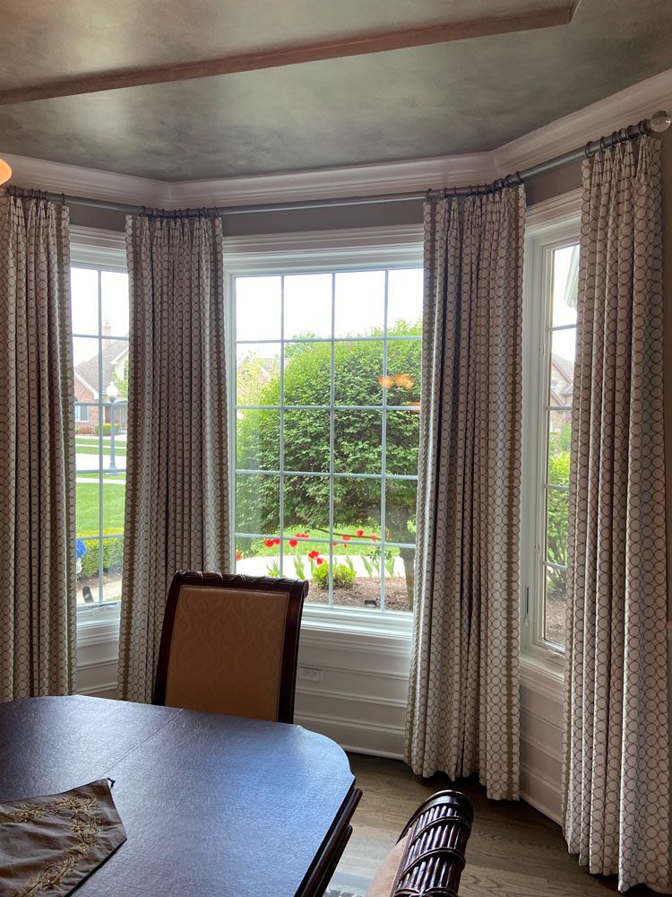 Dining room with bay windows, patterned curtains, and table.
