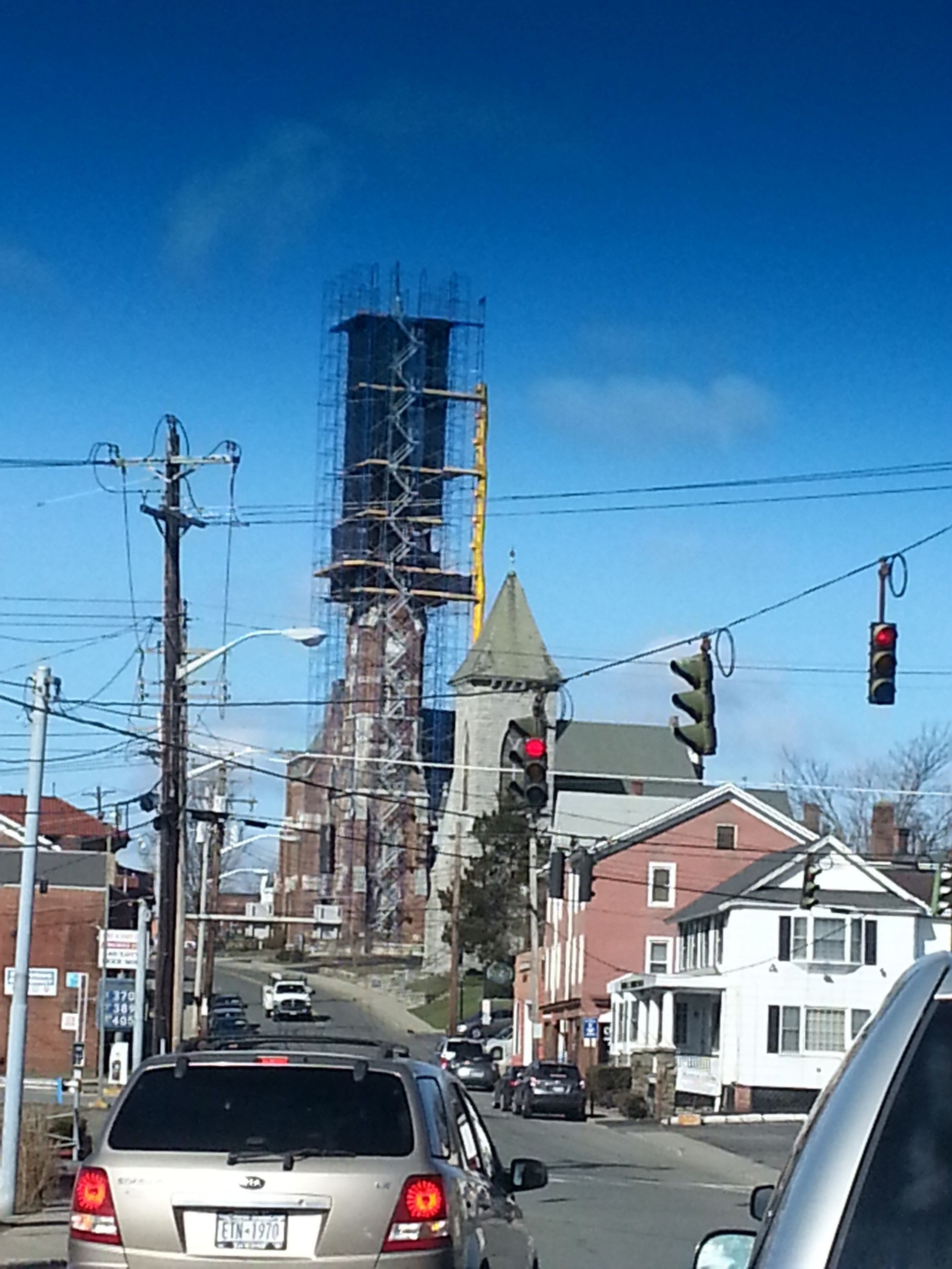 A tall church tower under construction, with scaffolding. Cars driving on the street in front.