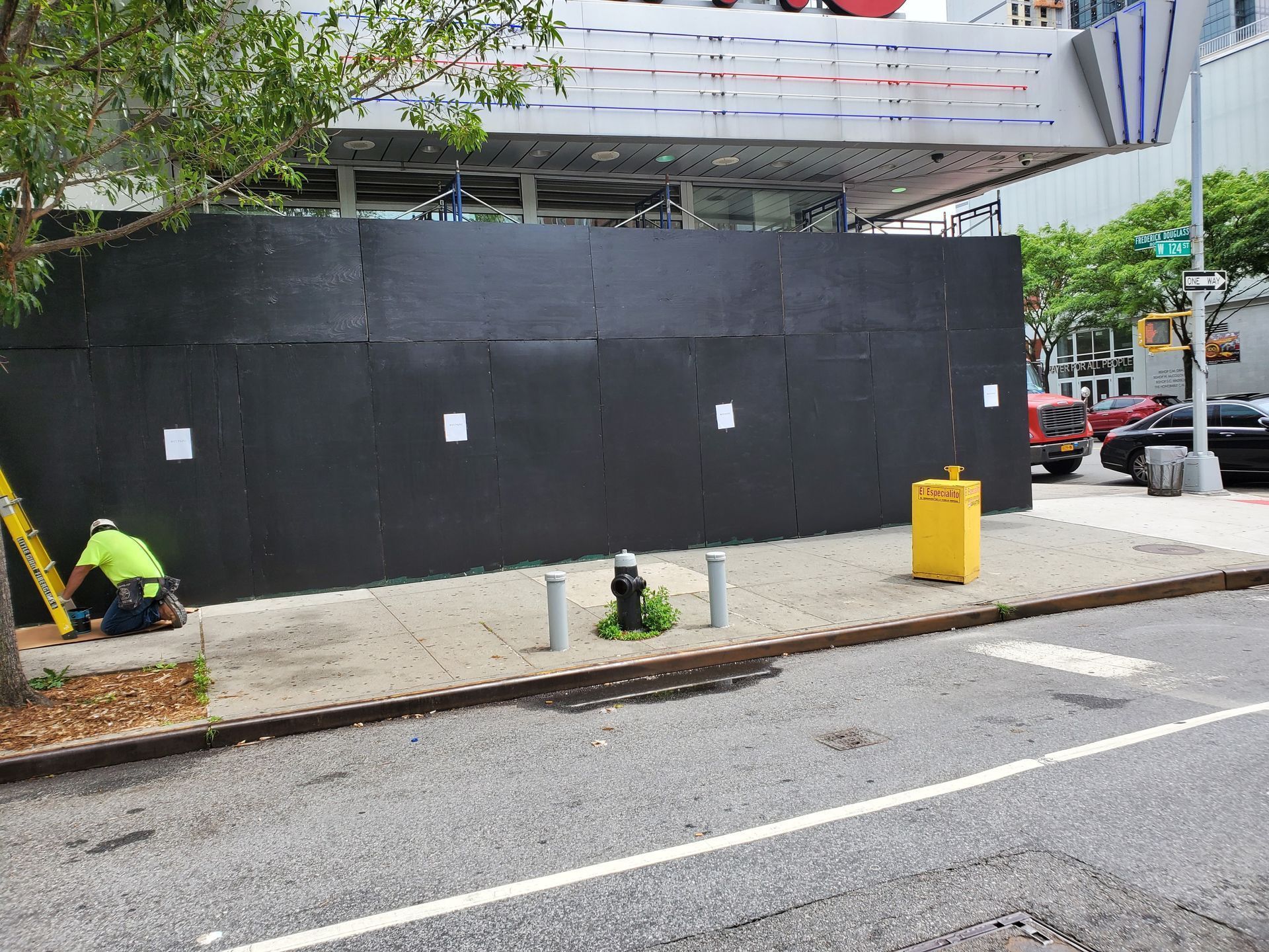 A black construction barrier blocks a gas station. A worker in safety gear works nearby.
