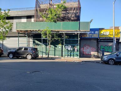 Street scene with a green-covered storefront, Subway sign, parked cars, and scaffolding.