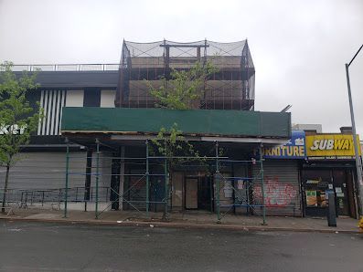 Building under construction with scaffolding, a Subway, and a furniture store on a city street.