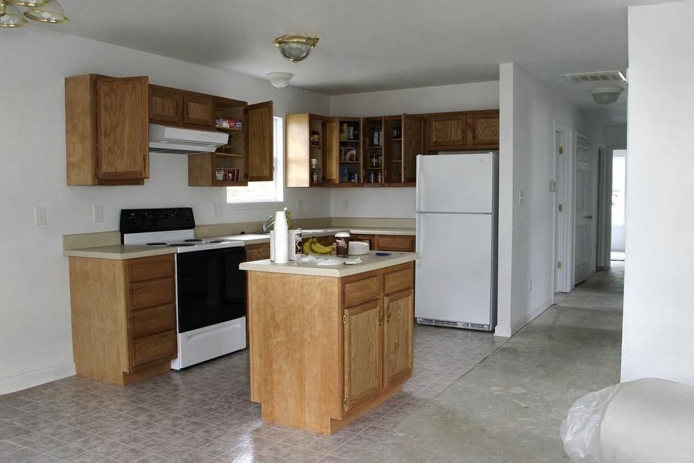 Kitchen with light wood cabinets, white appliances, and an island. Floors are gray.