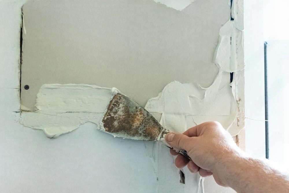 Person using a putty knife to apply drywall compound on a wall.