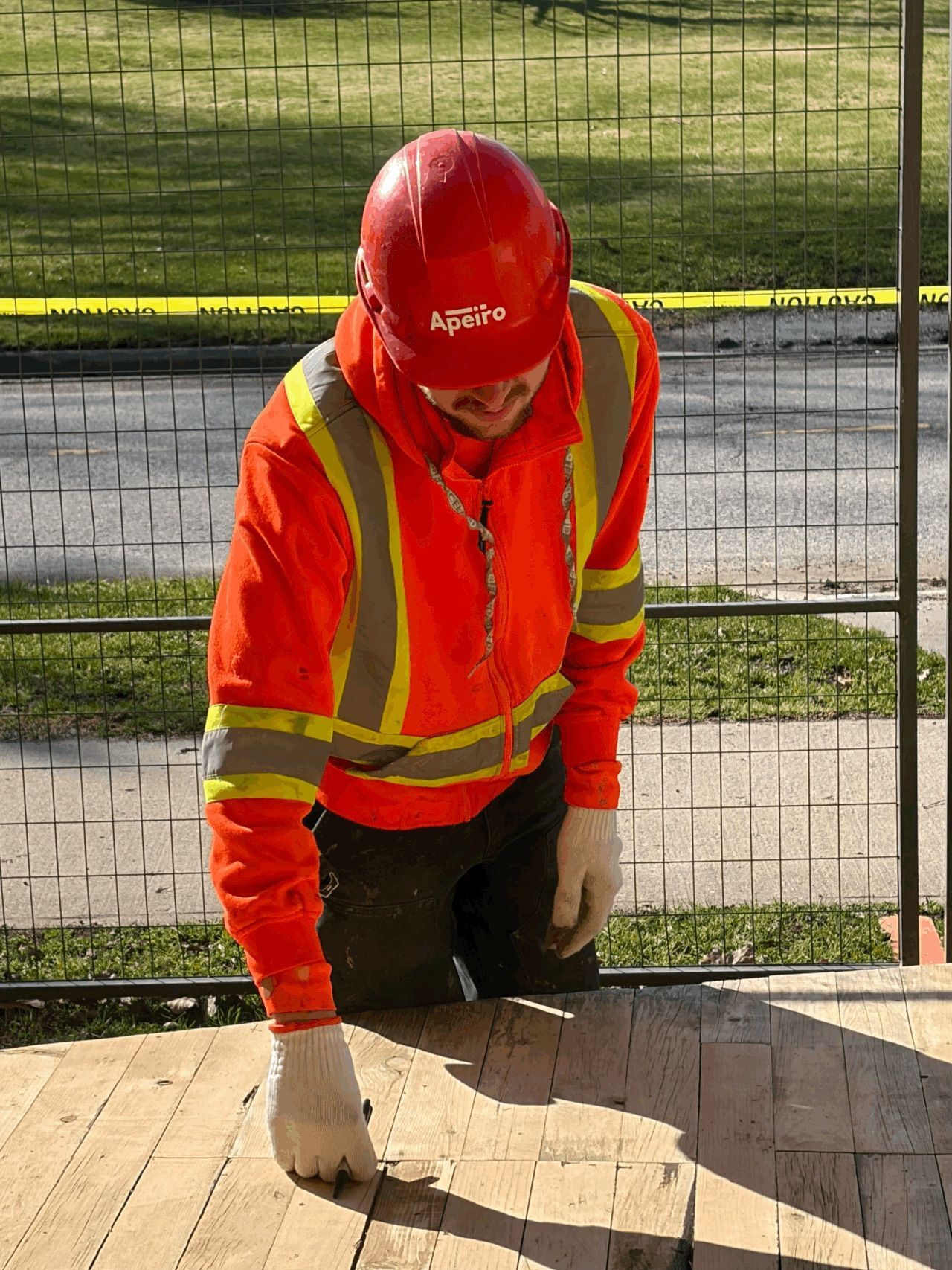 Worker in orange safety gear kneeling and measuring wood on a construction site