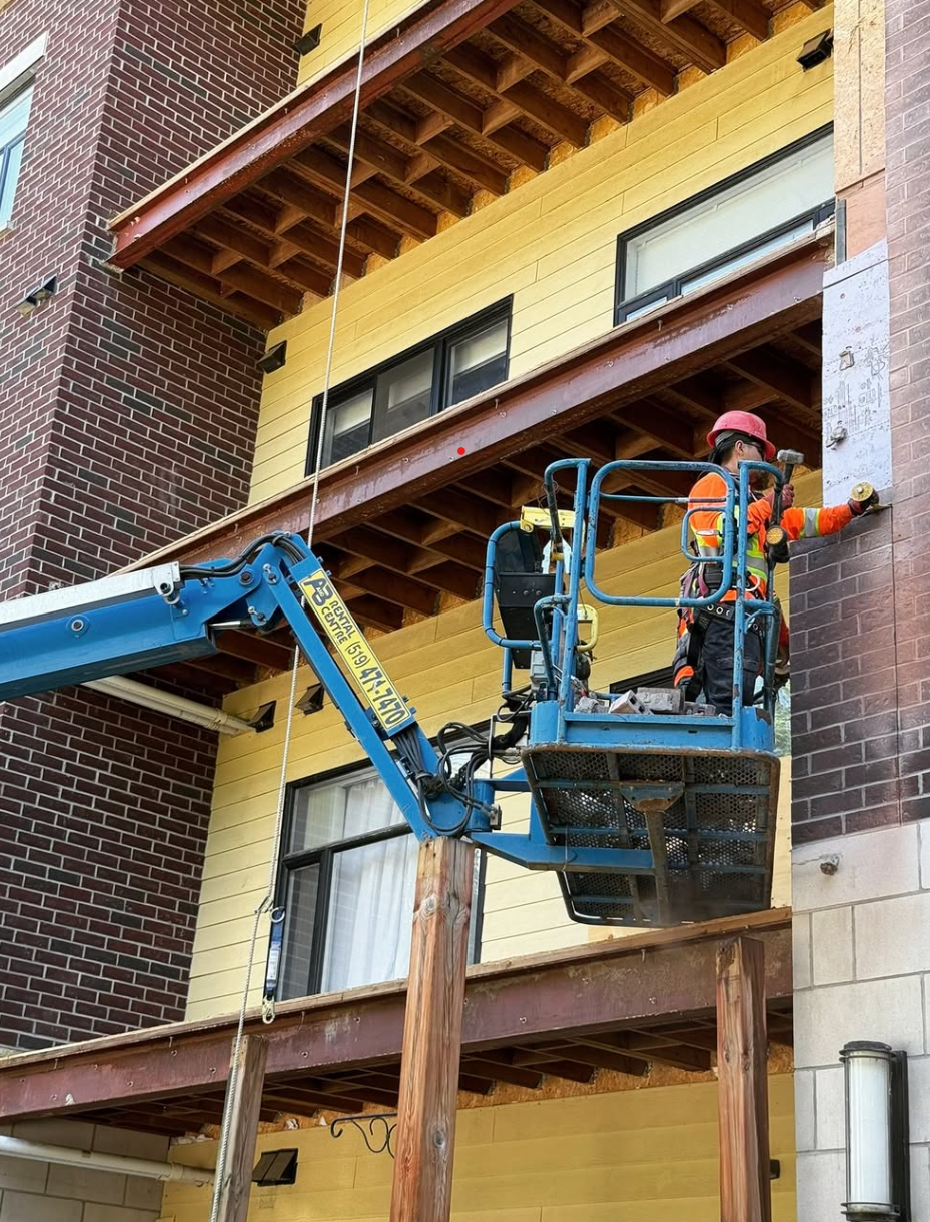 Worker in orange safety gear on a blue lift repairing a building wall