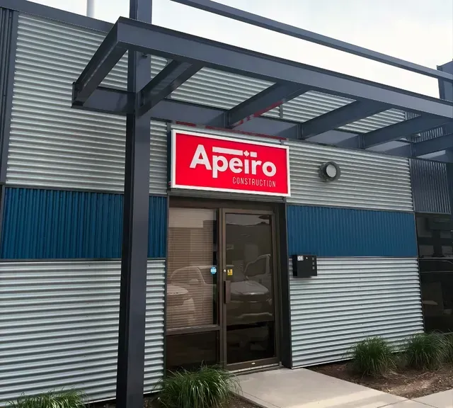 Apeiro storefront with red sign, glass entrance, and gray corrugated facade