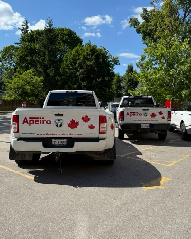 Three white trucks with Canadian flags parked in a lot, trees in the background on a sunny day.