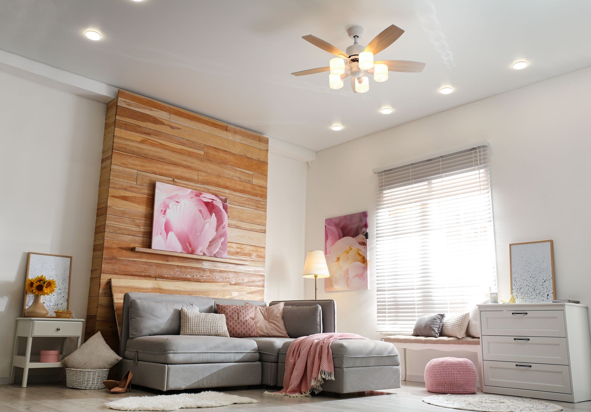 Cozy living room with gray sectional, wood accent wall, pink art, and a ceiling fan.