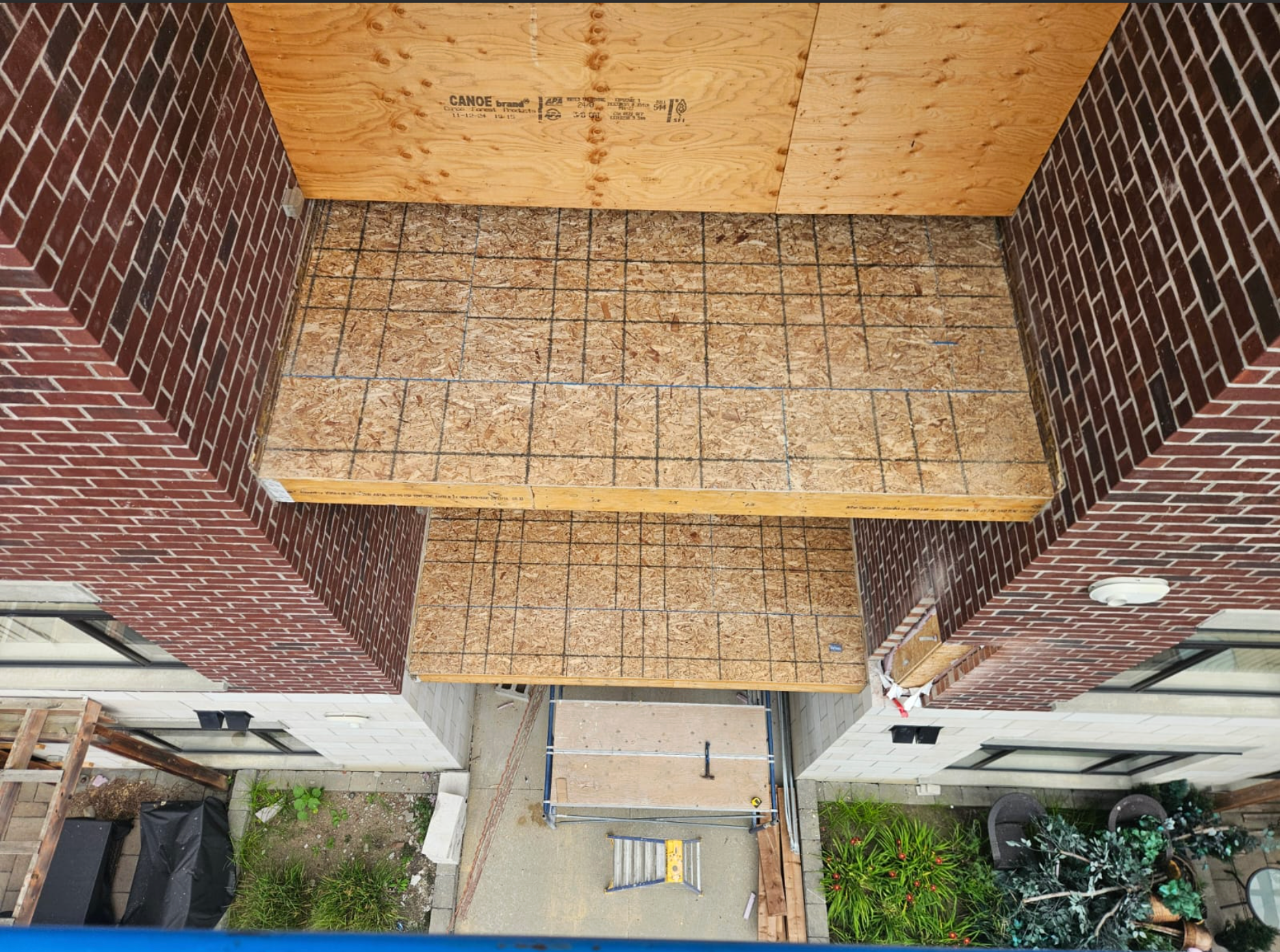 Top-down view of a building entrance with brick walls, tan awning, and a walkway below.
