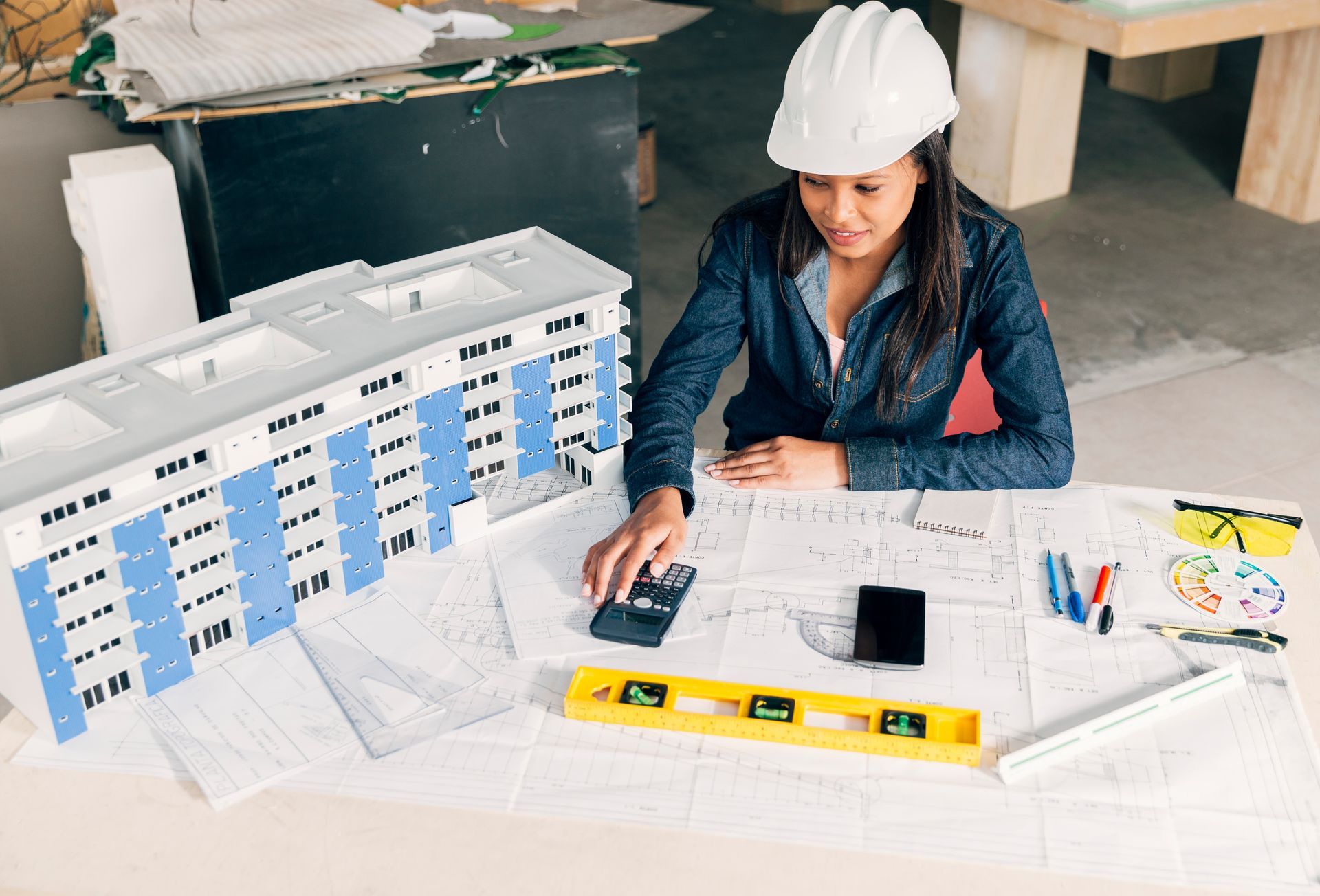 A woman in a hard hat is sitting at a table using a calculator.