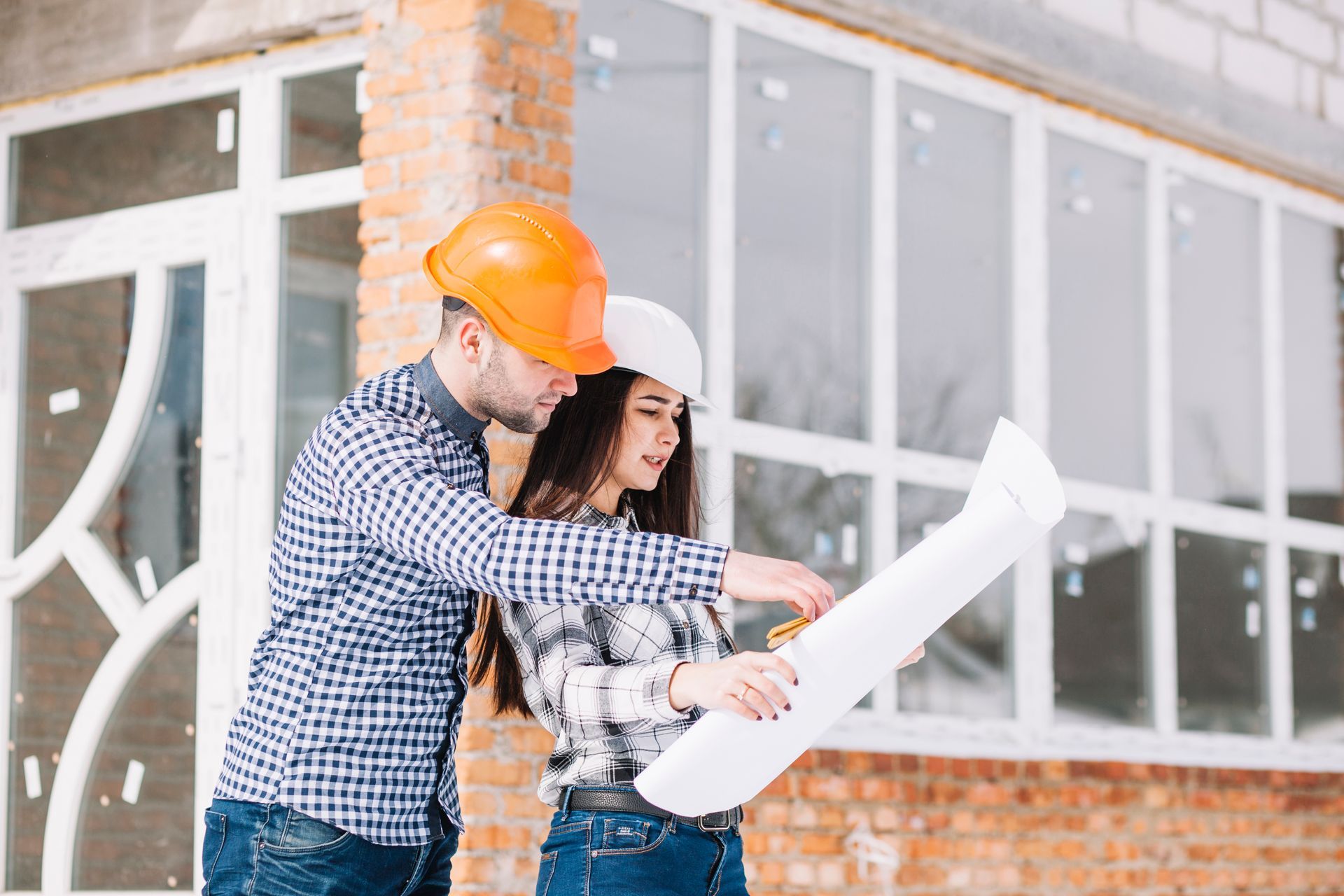 A man and a woman are looking at a blueprint in front of a building under construction.