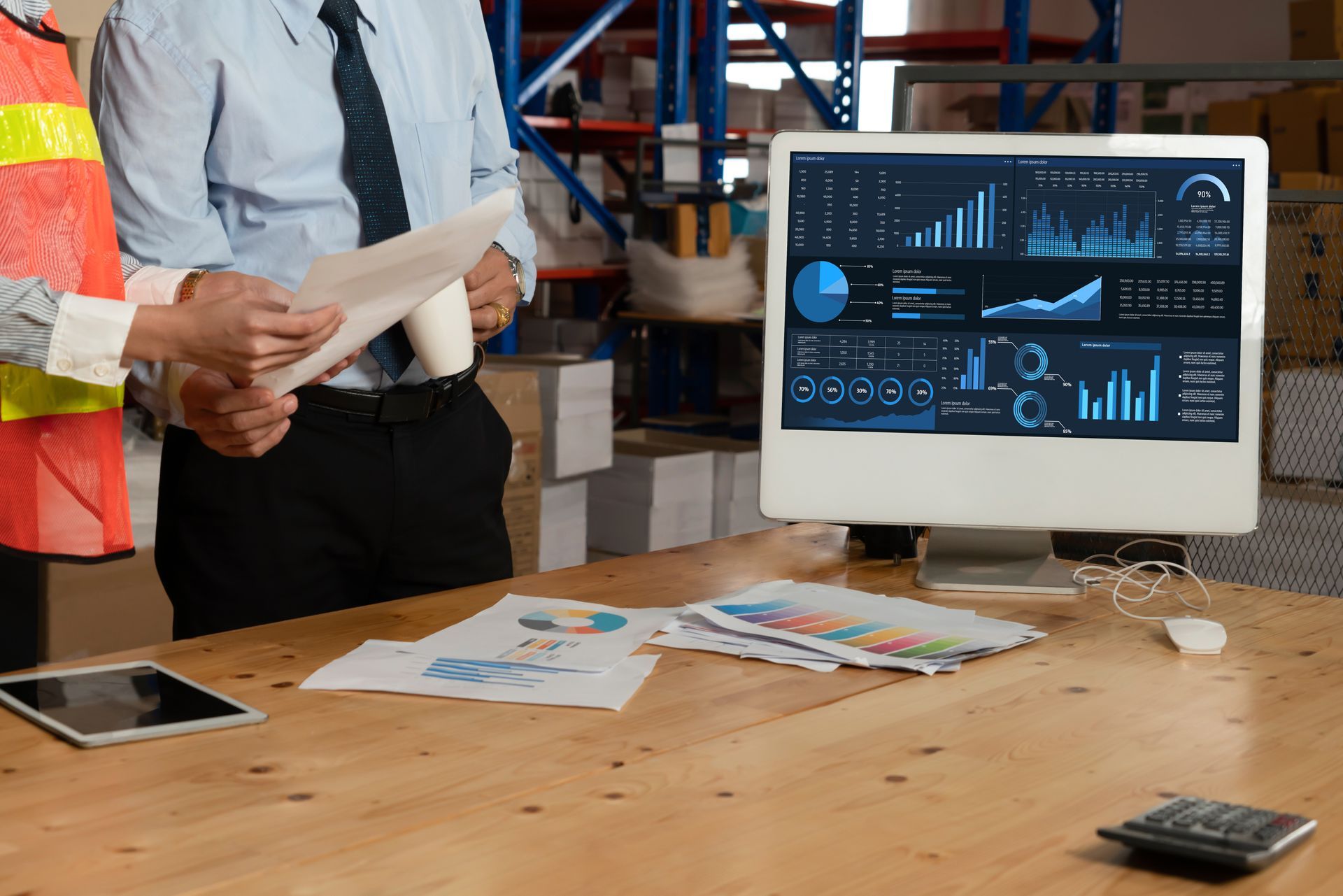 A man and a woman are standing in front of a computer in a warehouse.