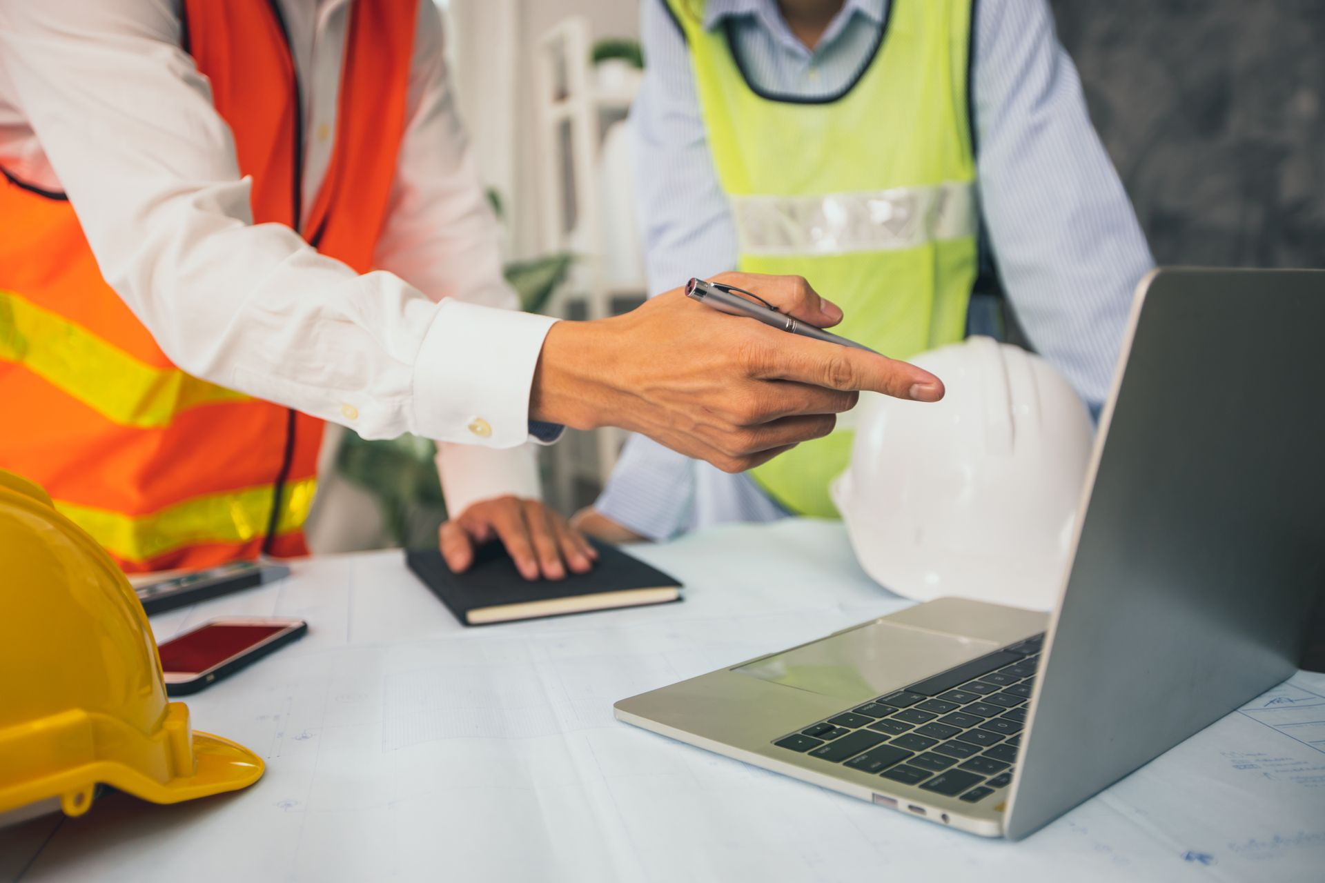 Two construction workers are looking at a laptop computer.