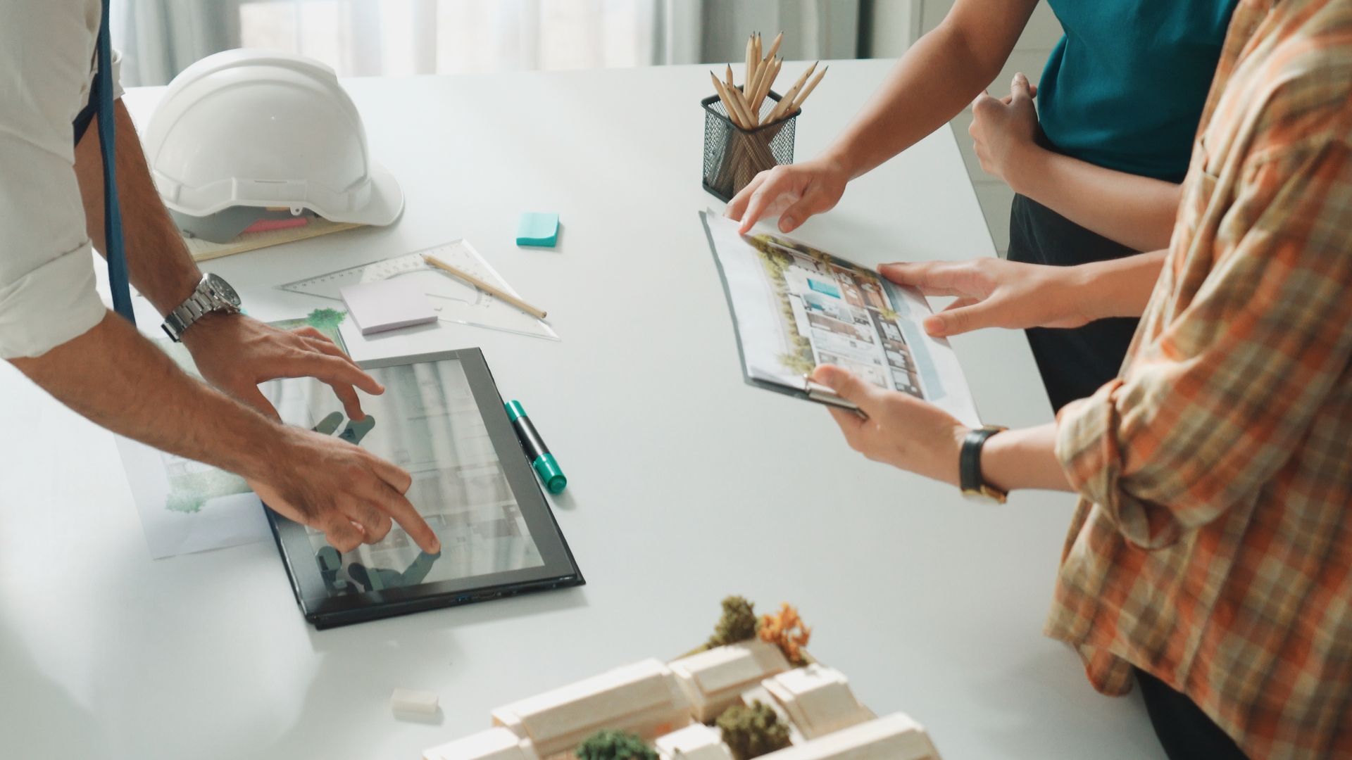 A group of people are sitting around a table looking at a tablet.