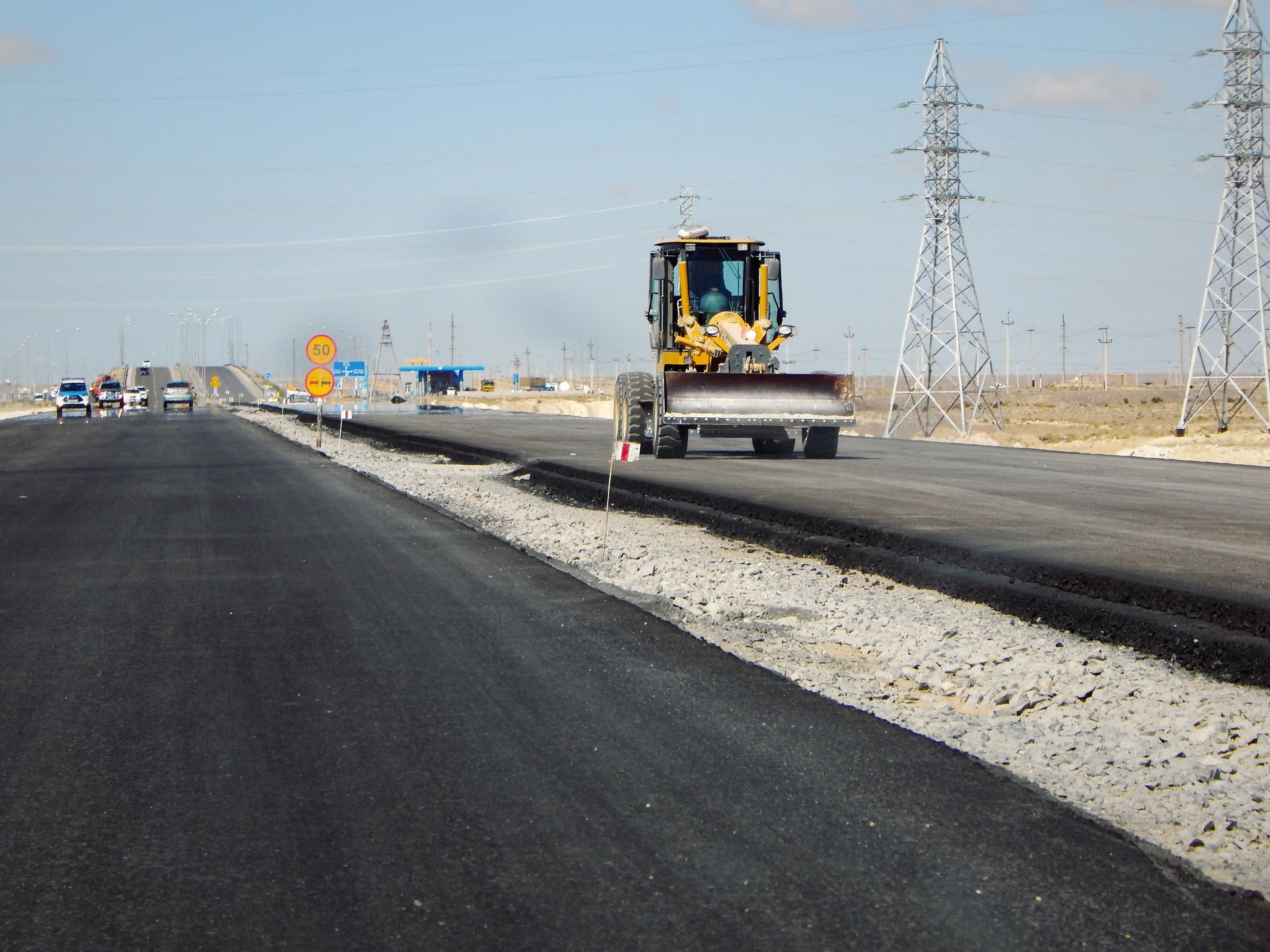 A bulldozer is driving down a road with power lines in the background