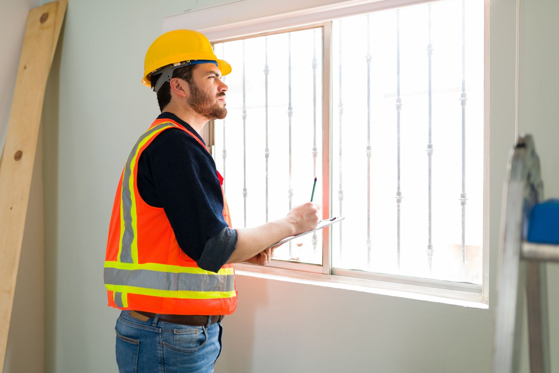 A construction worker is looking out of a window while holding a clipboard.