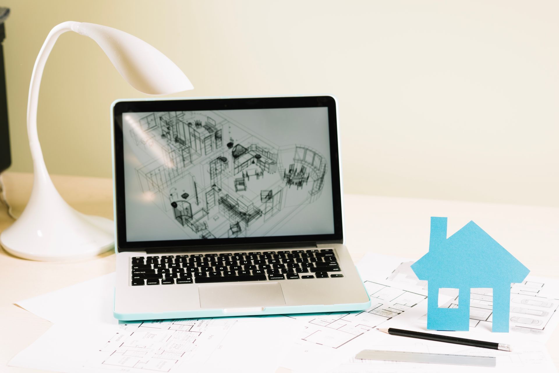 A laptop computer is sitting on a desk next to a lamp and a house.