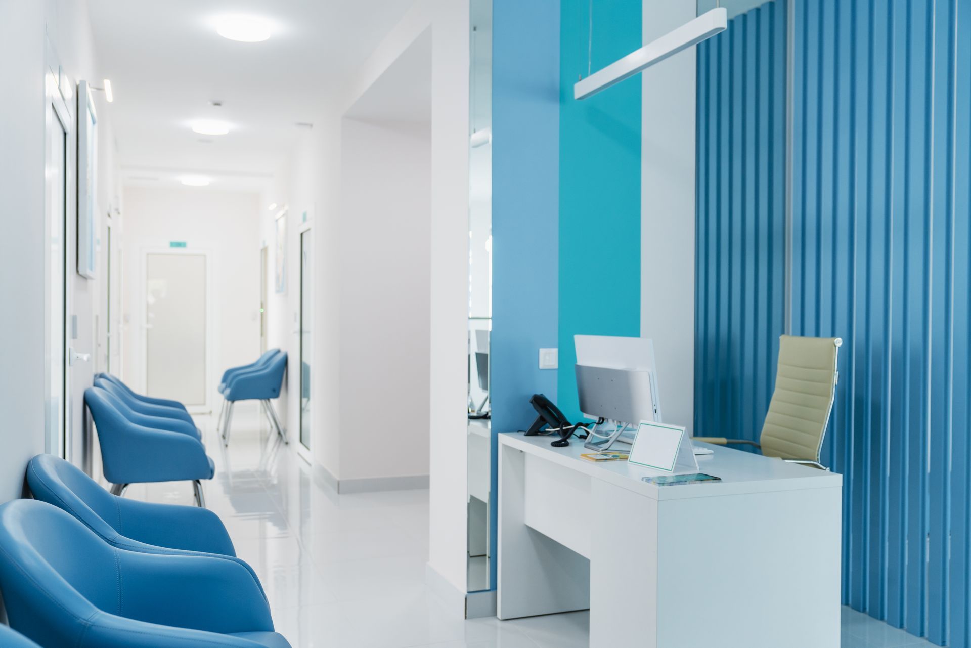 A waiting room in a hospital with blue chairs and a desk.