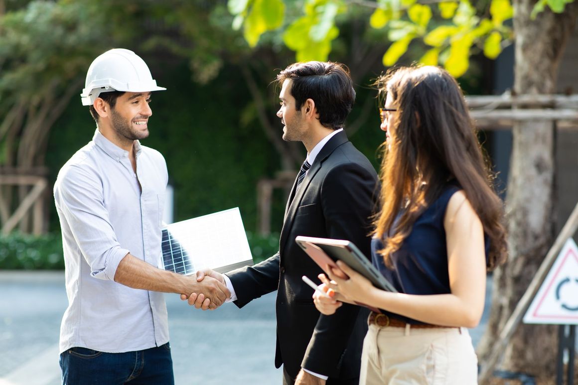 A man and a woman are shaking hands with a man wearing a hard hat.
