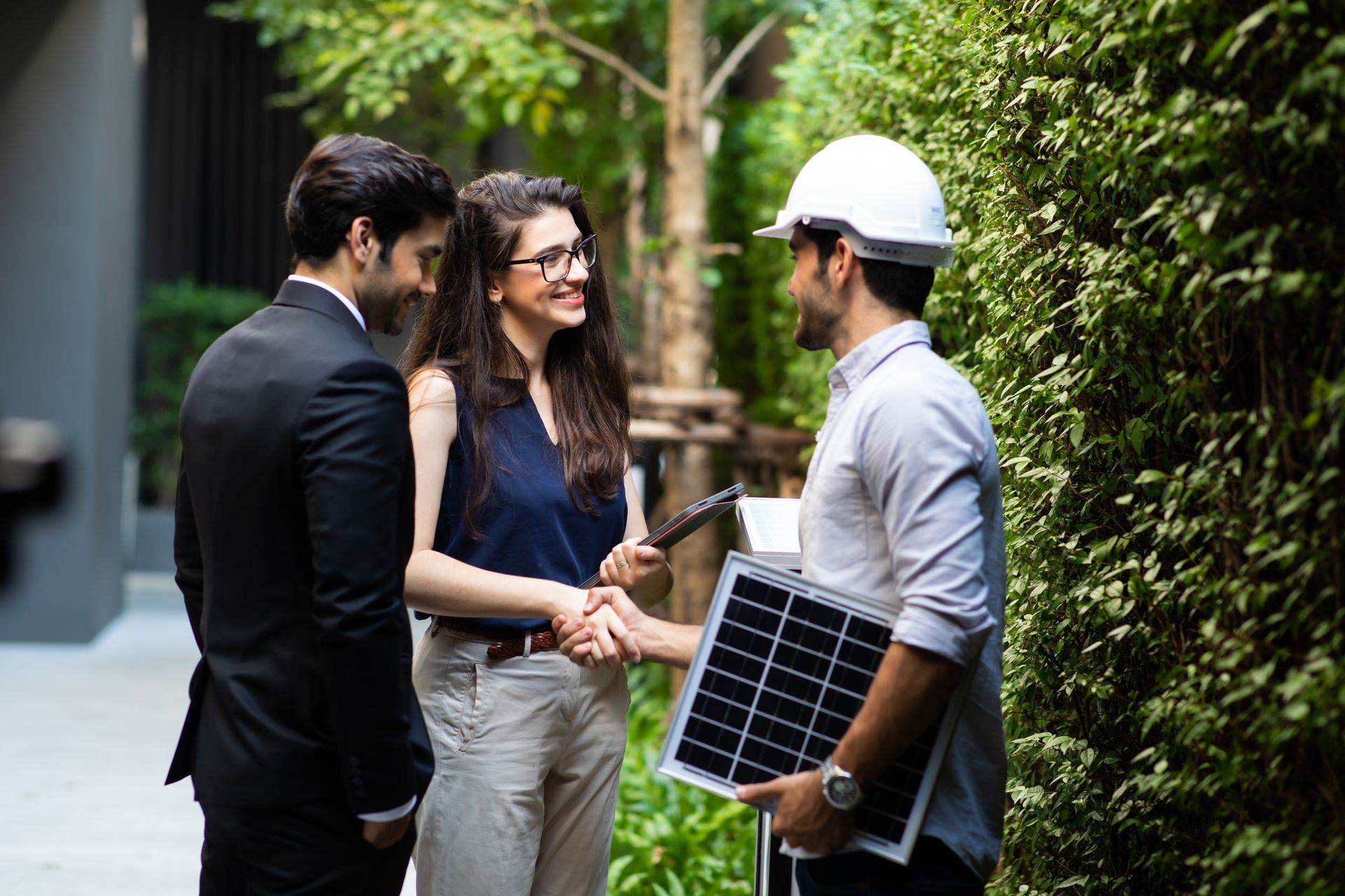 A man and a woman are shaking hands with a man holding a solar panel.