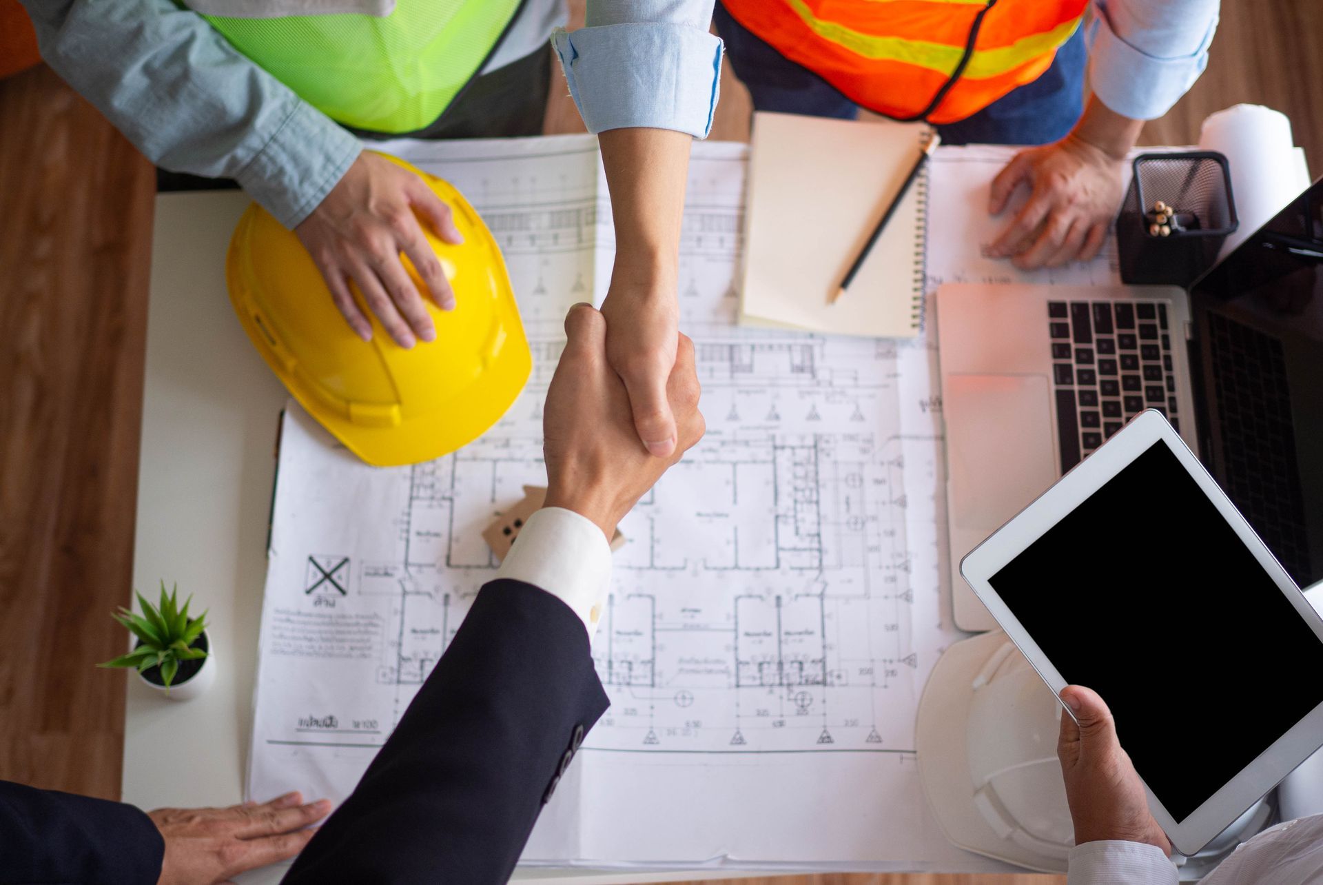 A group of construction workers are shaking hands over a blueprint.