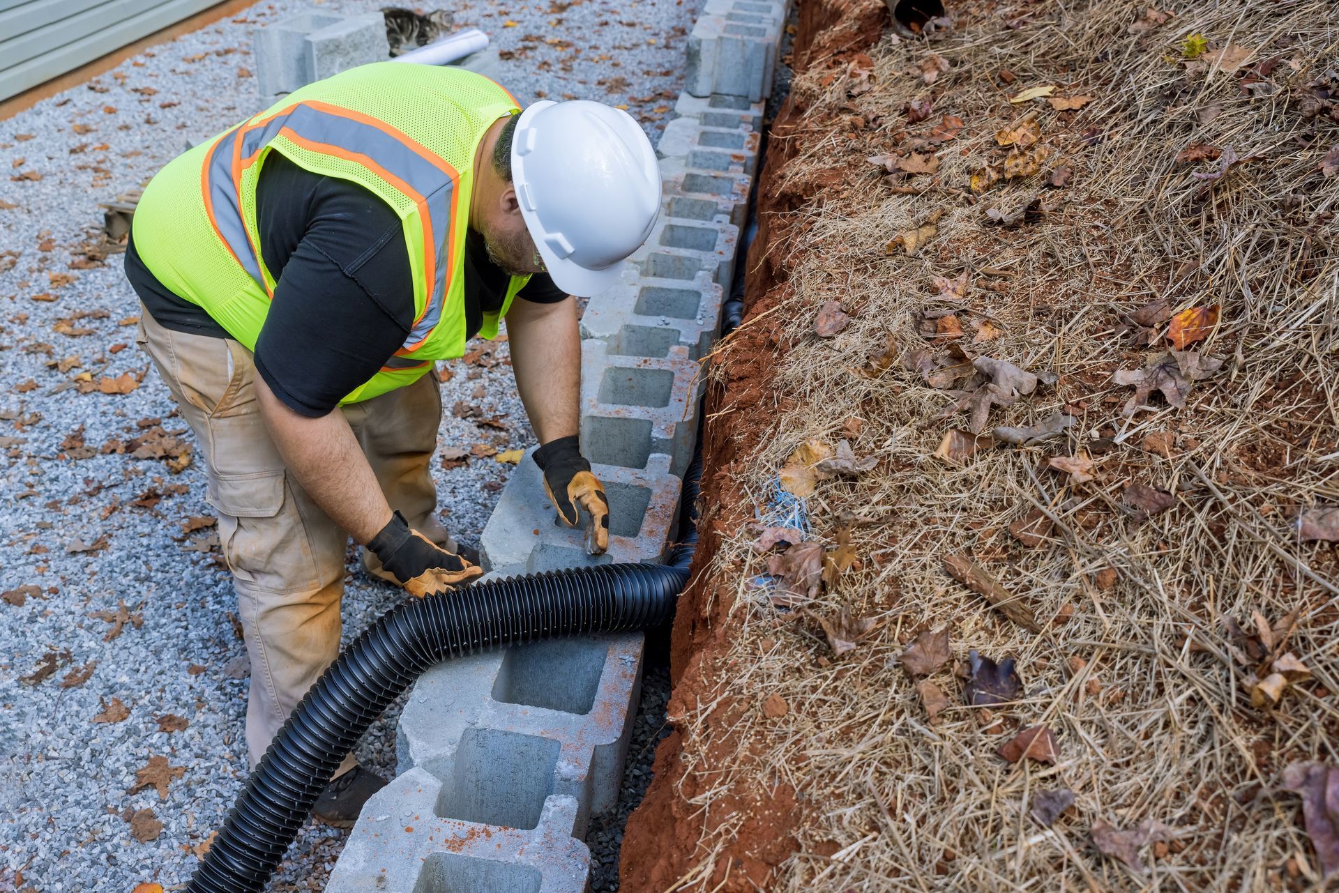 A construction worker is working on a drainage system on a brick wall.
