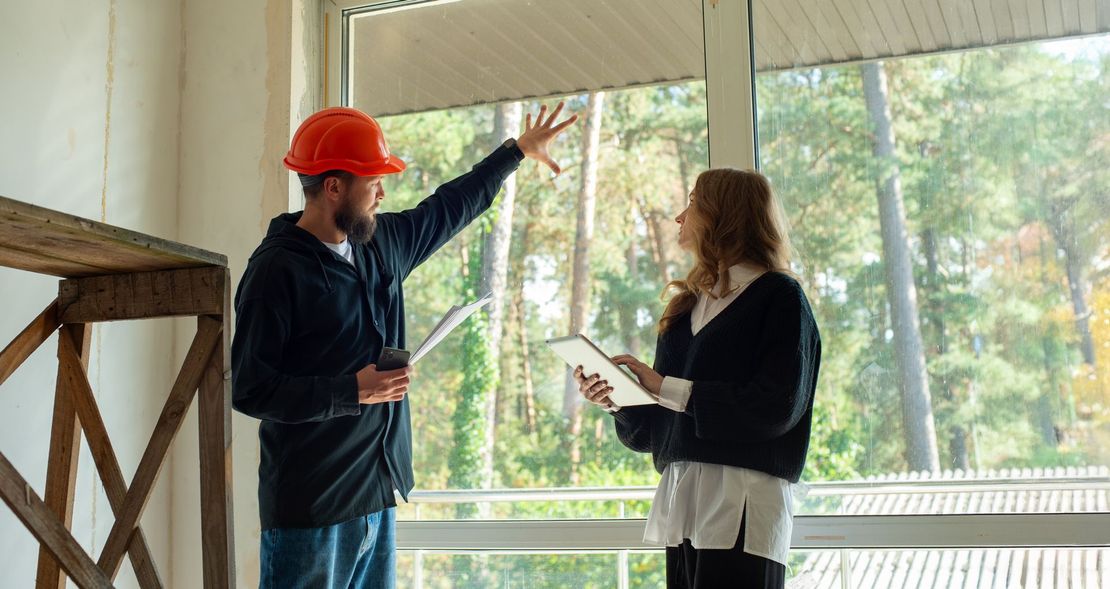 A man and a woman are standing next to each other in a room looking out a window.