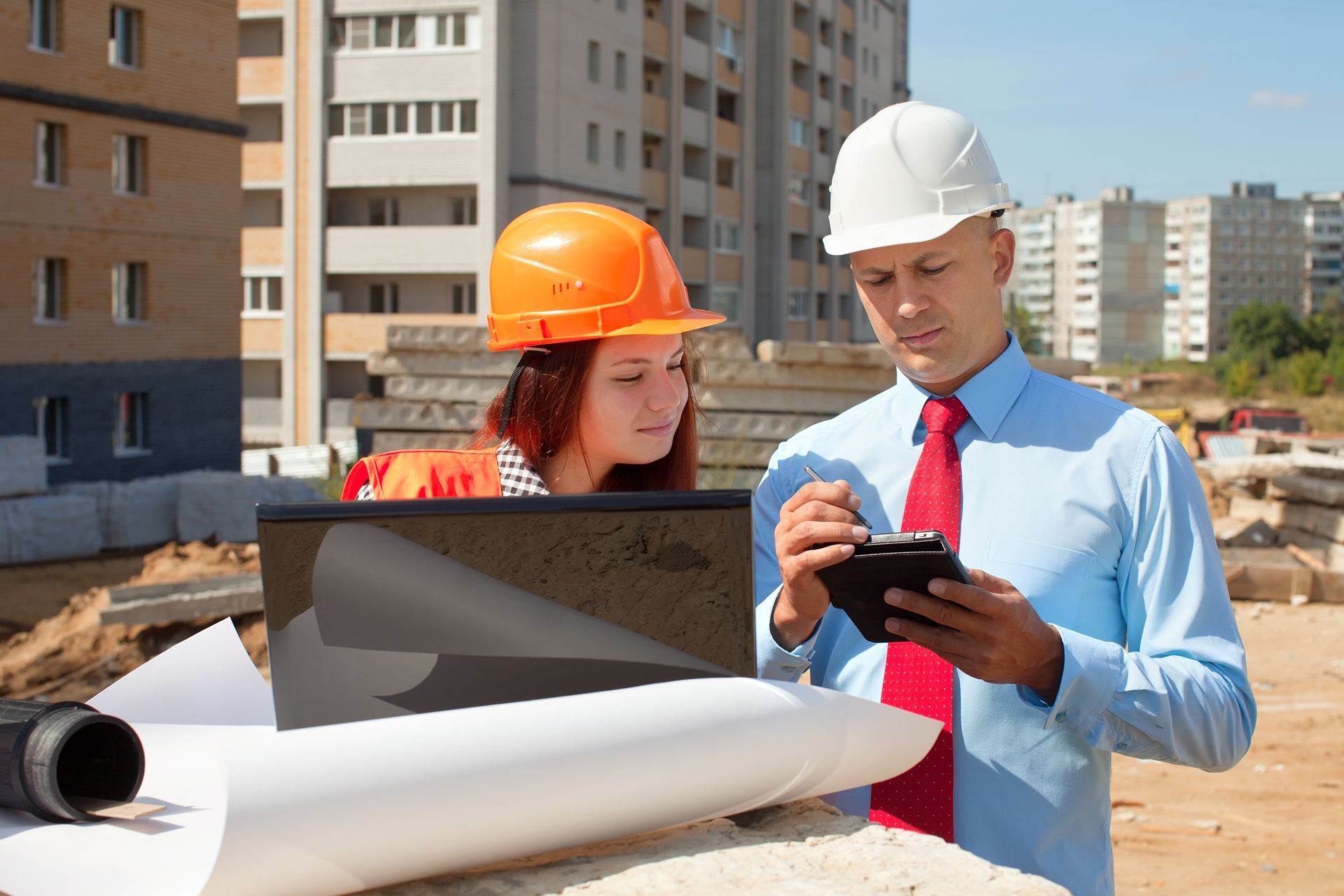 A man and a woman are looking at a laptop on a construction site.